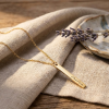 Gouden rechthoekige staafvormige hanger met naam gravure aan gouden ketting liggend op linnen doek met lavendel lifestyle modelfoto gepersonaliseerd gouden naamketting sieraad