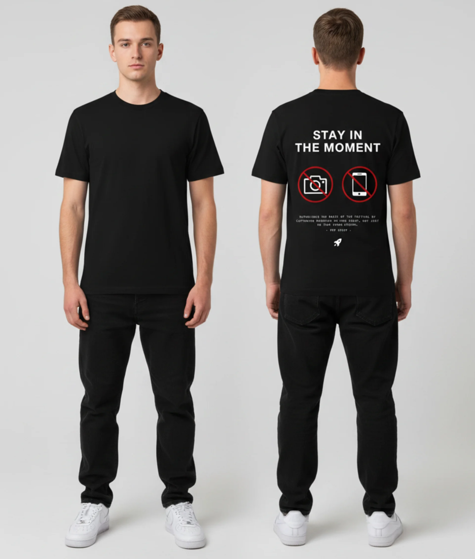 Zwart unisex T-shirt voor- en achteraanzicht gedragen door mannelijk model met Stay in the Moment print doorgestreepte camera en telefoon icoontjes op de rug