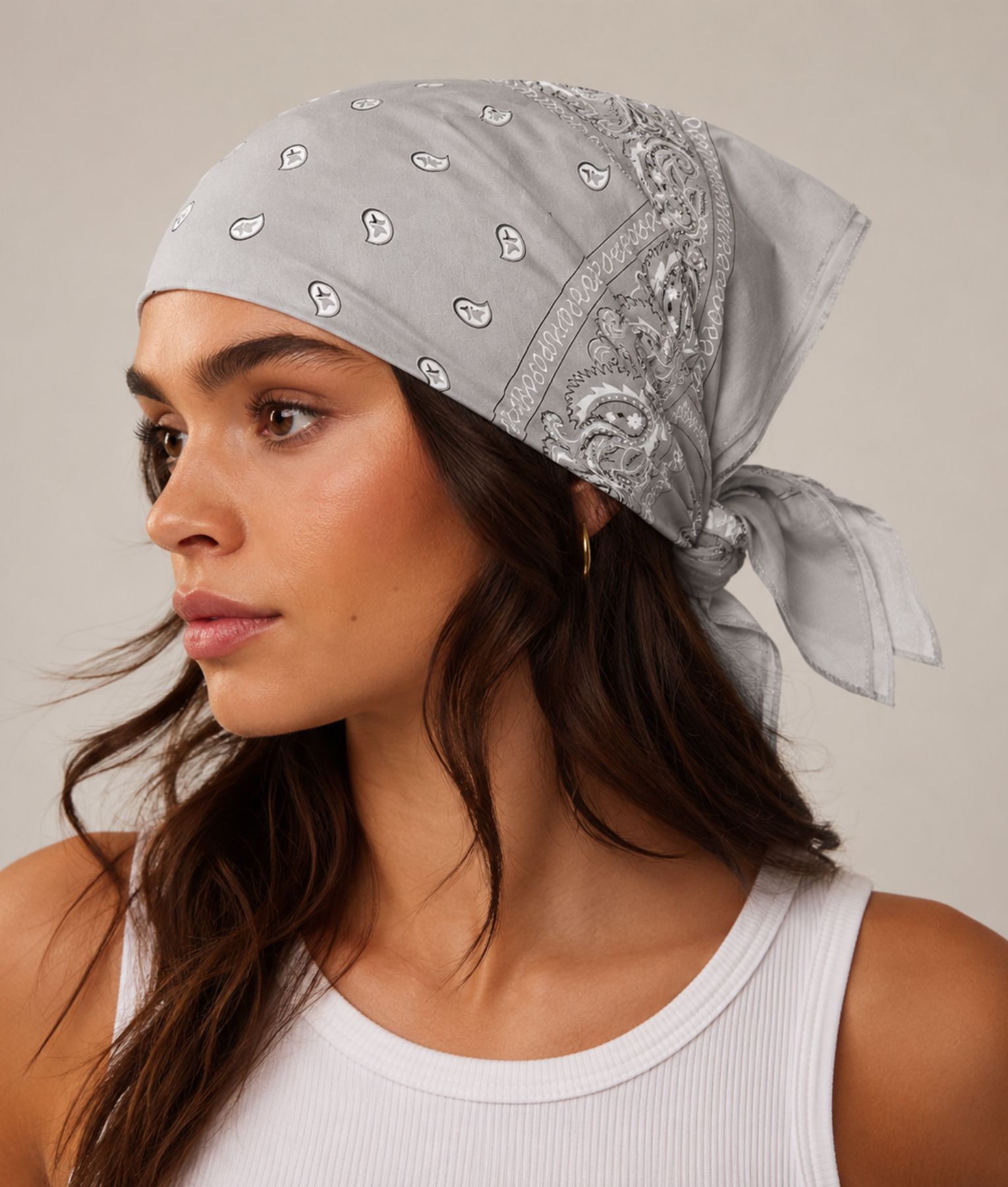 Grijze bandana gedragen door model – klassieke paisley bandana in grijs met witte print, gedragen als hoofddoek. Veelzijdig te stylen als haarband, nekdoek of accessoire. Ideaal als cadeau of festival- en zomeraccessoire.