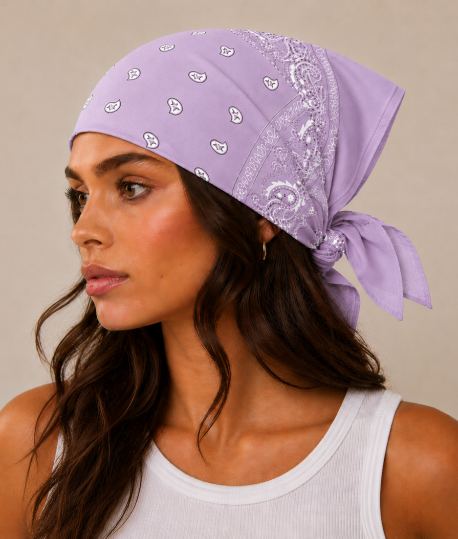 Lila lichtpaarse bandana gedragen door model – klassieke paisley bandana in lila lichtpaars met witte print, gedragen als hoofddoek. Veelzijdig te stylen als haarband, nekdoek of accessoire. Ideaal als cadeau of festival- en zomeraccessoire.