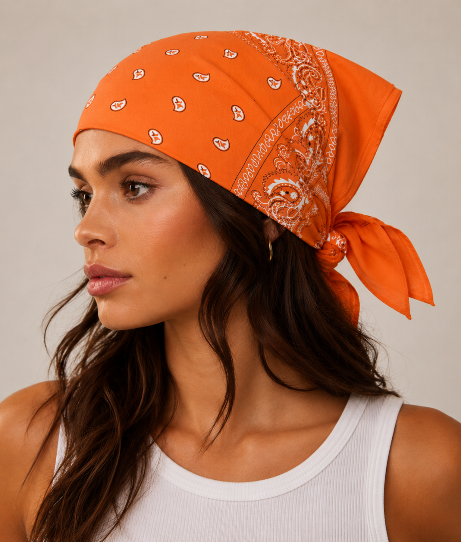 Oranje bandana gedragen door model – klassieke paisley bandana in oranje met witte print, gedragen als hoofddoek. Veelzijdig te stylen als haarband, nekdoek of accessoire. Ideaal als cadeau of festival- en zomeraccessoire.