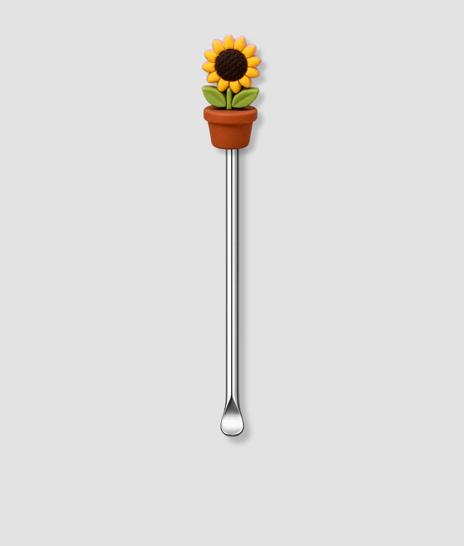 Mini schepje cocktailstirrer met zonnebloem figuur in bruine terracotta bloempot met groene bladeren bovenop en zilveren steel
