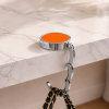 Oranje opvouwbare tassenhanger aan tafel met handtas