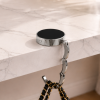 Zwarte opvouwbare tassenhanger aan tafel met handtas