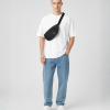 Man met zwarte crossbody fanny pack over wit oversized T-shirt en blauwe jeans