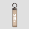 Beige suède sleutelhanger verticaal model met metalen ring en voorbeeldtekst 'CUSTOM'