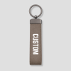 Taupe suède sleutelhanger verticaal model met metalen ring en voorbeeldtekst 'CUSTOM'