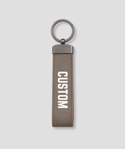 Taupe suède sleutelhanger verticaal model met metalen ring en voorbeeldtekst 'CUSTOM'