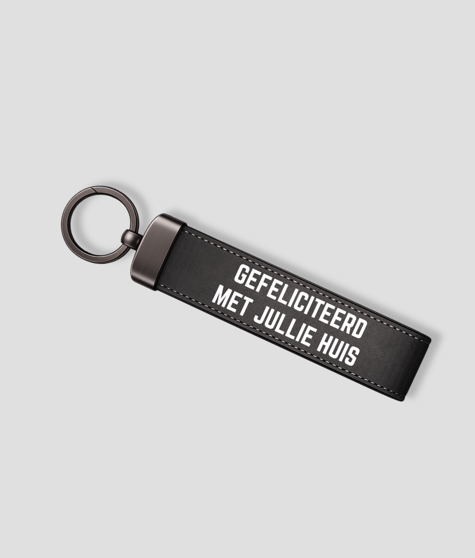 Antracietkleurige suède sleutelhanger met metalen ring en tekst 'GEFELICITEERD MET JULLIE HUIS'
